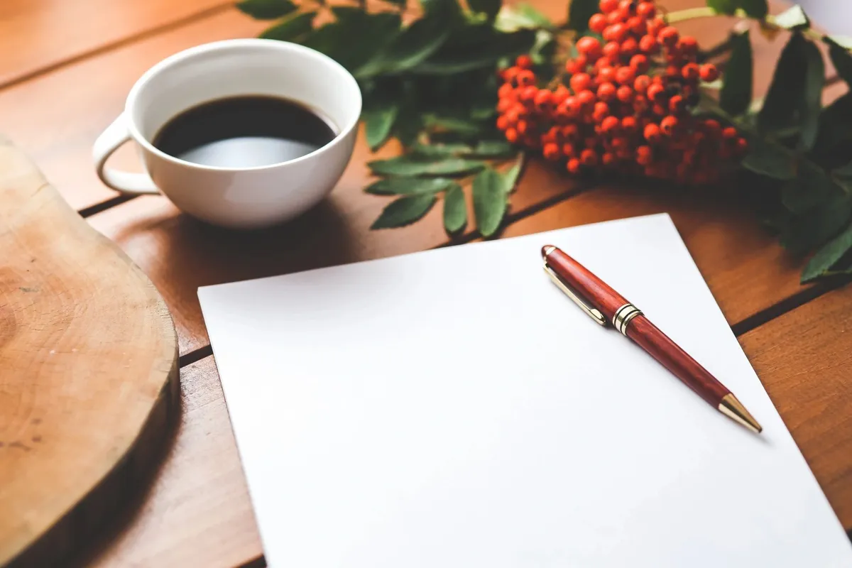Cup of coffee, a blank sheet of paper and a red pen on a wooden table